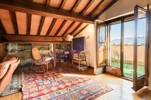A spacious room with a large window, a wooden ceiling, a television, and a patterned rug.
