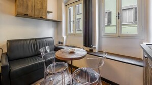 En modern inredning med en svart lädersoffa, ett runt träbord och stolar i genomskinligt glas.