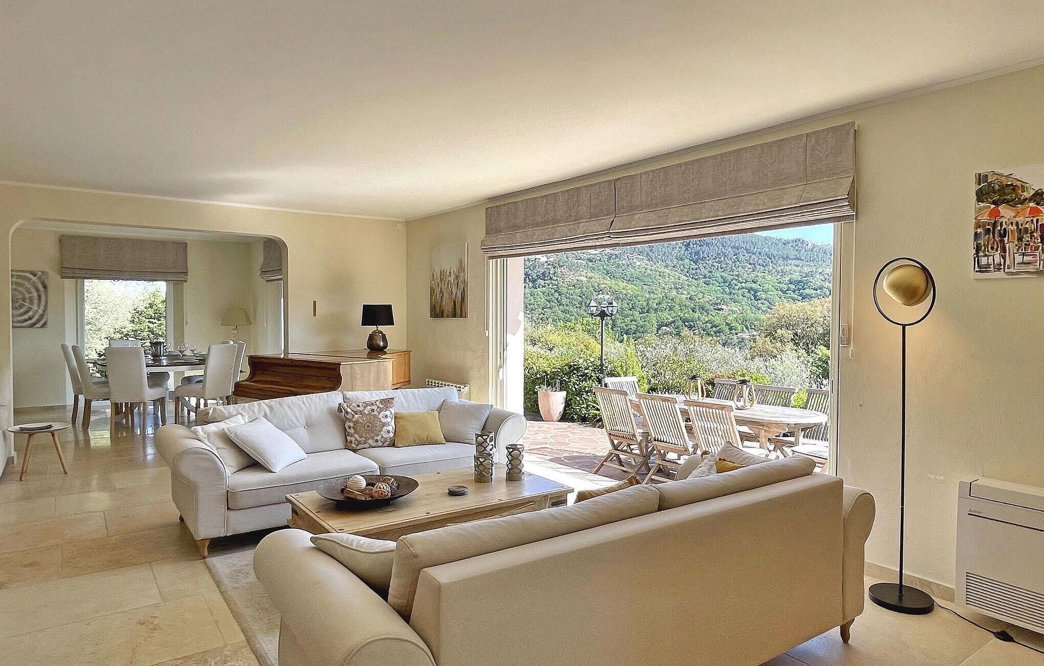 A spacious living room with a large window offering a view of a mountainous landscape. There is a dining area with a table and chairs visible in the background.