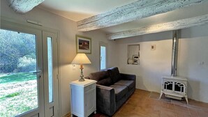 Een gezellige kamer met een bank, een klein tafeltje met een lamp, een wit kastje en een witte kookplaat.