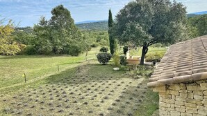 A stone building with a tiled roof, surrounded by a grassy field with scattered trees and a distant view of hills.