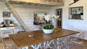 A dining area with a wooden table, clear chairs, a white orchid centerpiece, and a chandelier.