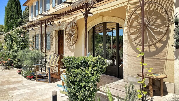 A traditional building with large wooden wheels attached to the exterior walls, a stone pathway, and a variety of plants and flowers.