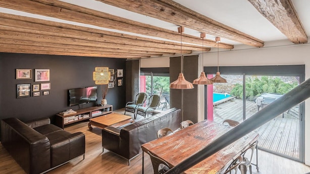 A modern living room with a wooden ceiling, a TV, a coffee table, and a dining area with a wooden table and chairs.