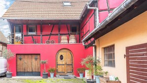 A two-story building with a red facade, a wooden door, and multiple potted plants.