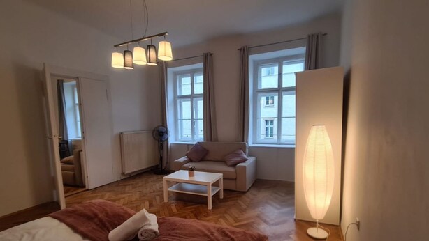 Hotellihuone, jossa on sänky, sohva, sohvapöytä, lattiavalaisin ja suuret ikkunat.