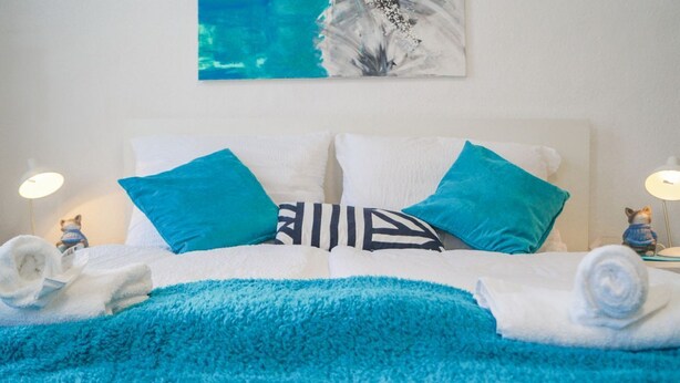 Una cama con una manta azul, almohadas blancas y una almohada azul.