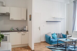 Une cuisine moderne avec des meubles blancs, un plan de travail et un évier. On y trouve un canapé bleu avec des coussins, une petite table et un tapis à motifs.