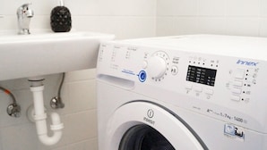 Una lavadora de carga frontal con panel de control digital, un lavamanos blanco y un dispensador de jabón.
