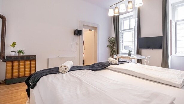 A hotel room with two beds, a desk, a TV, and a large window.