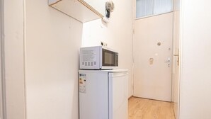 A compact kitchen with a white refrigerator and microwave, a wooden floor, and a closed door.