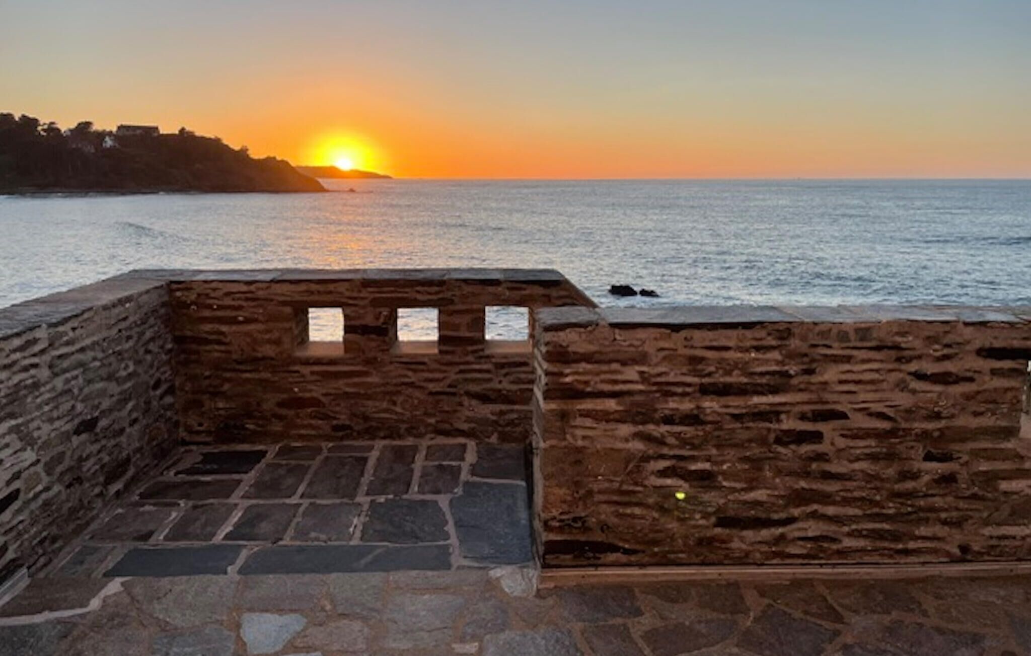 Mural de pedra com vista para o pôr do sol sobre o mar.