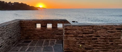A stone wall with a view of the sunset over the sea.