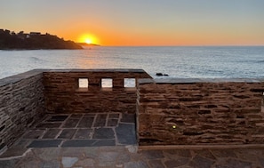Mural de pedra com vista para o pôr do sol sobre o mar.