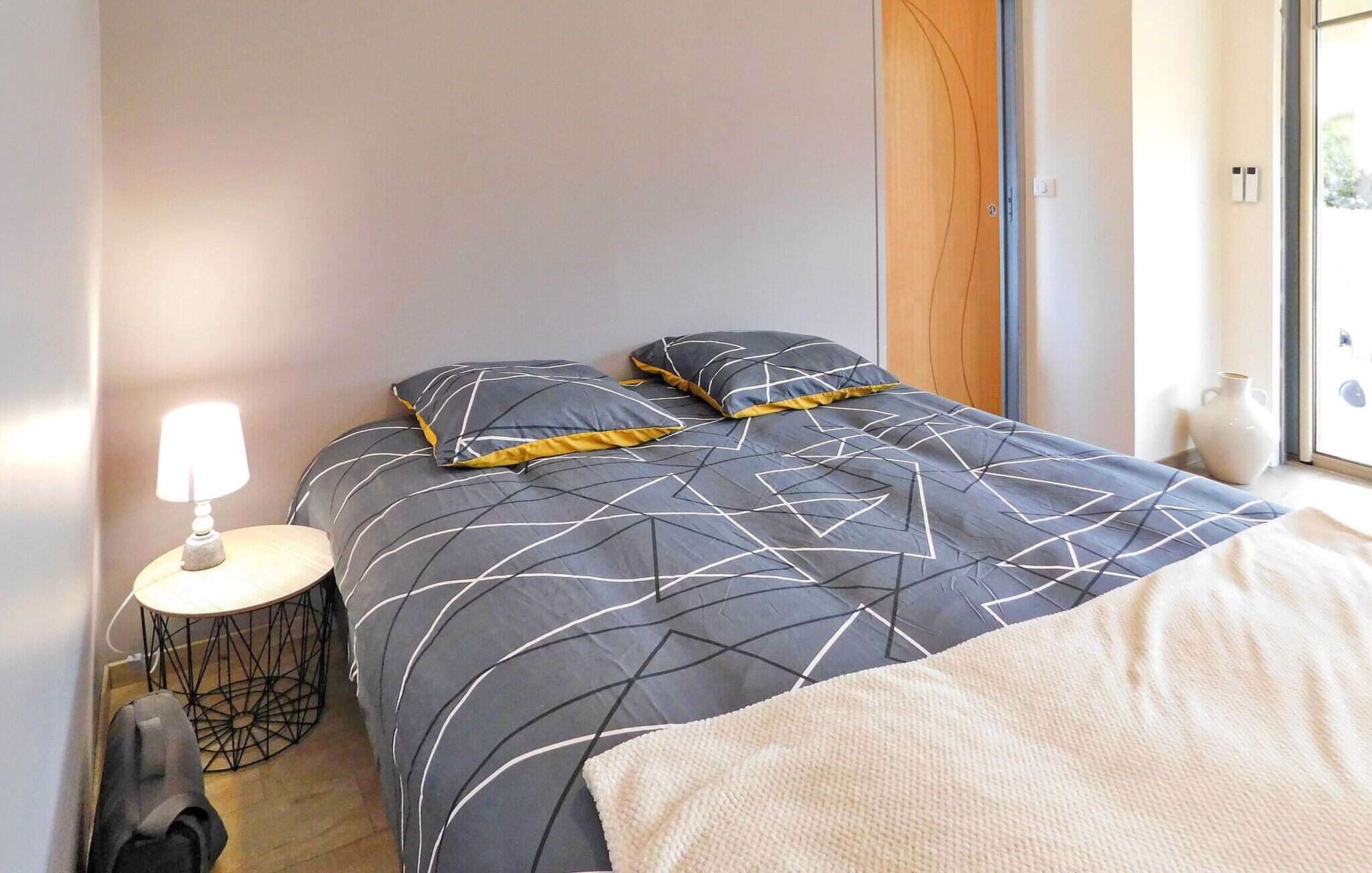 A bedroom with a bed, a bedside table with a lamp, and a window.