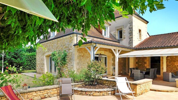 Une maison en pierre dotée d’un patio couvert, d’un espace salon extérieur et d’un jardin.