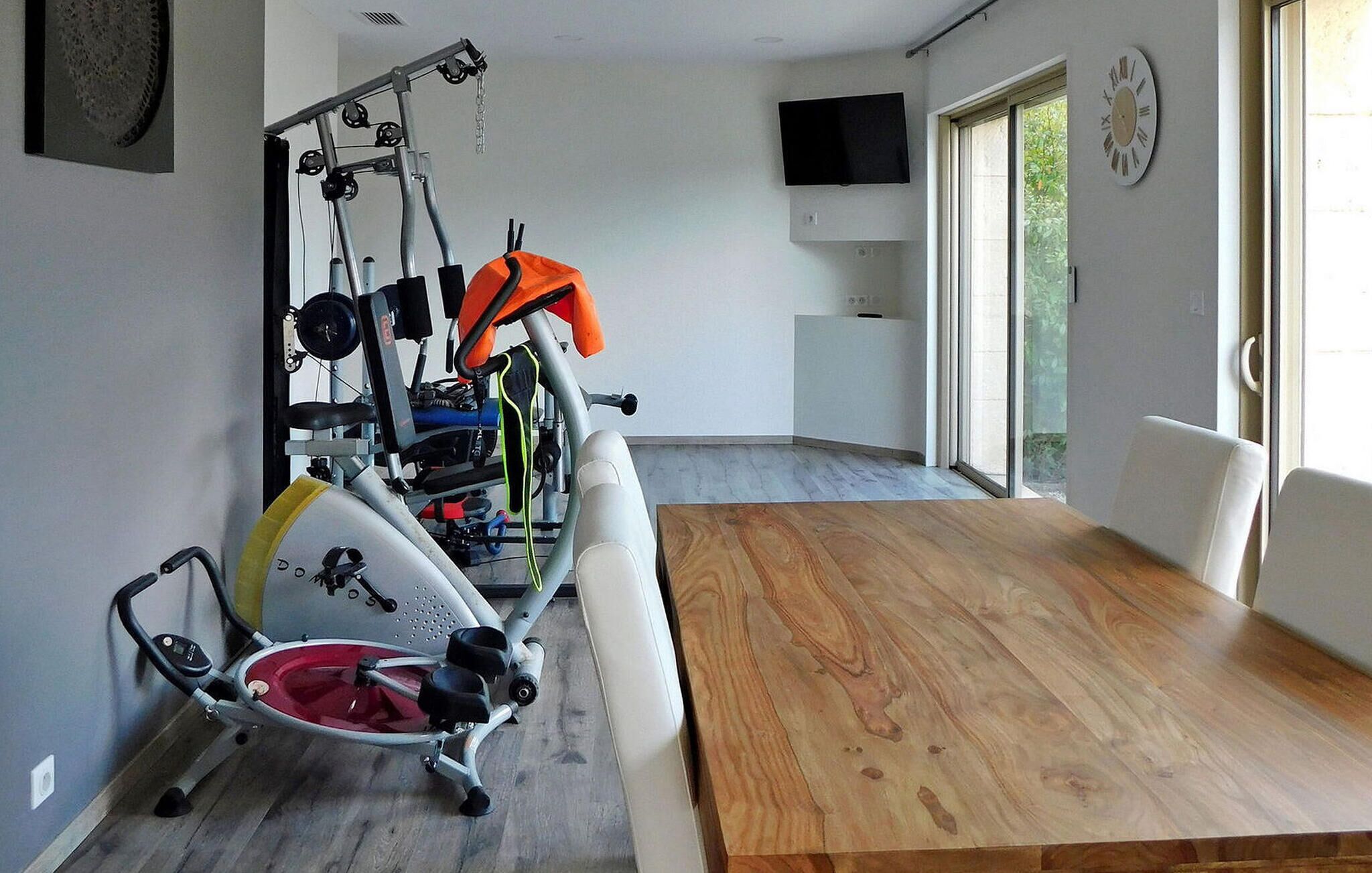 A home gym with exercise equipment, a dining table, and a TV mounted on the wall.