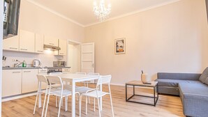 Eine moderne Küche mit weißen Schränken, einem Esstisch mit Stühlen, einem grauen Sofa und einer Deckenleuchte.