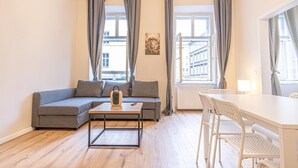 Ein modernes Wohnzimmer mit Sofa, Couchtisch, Esstisch mit Stühlen und großen Fenstern mit Vorhängen.