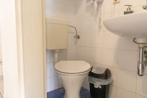 A bathroom with a toilet, a sink, and a trash bin.
