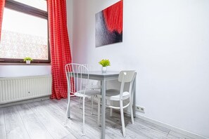 A room with a white table and chairs, a window with a red curtain, a radiator, and a wall-mounted artwork. - Modern Apart. - Huge Longstay discount (Vienna)