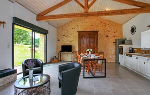 A spacious living area with a dining table, comfortable seating, a kitchen with modern appliances, and a large window offering a view of the outdoors.