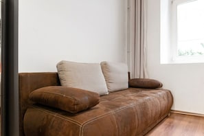 Un sofá de cuero marrón con cojines en una habitación con ventana y suelo de madera.