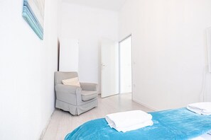 A bedroom with a bed, a chair, a wardrobe, and a door.