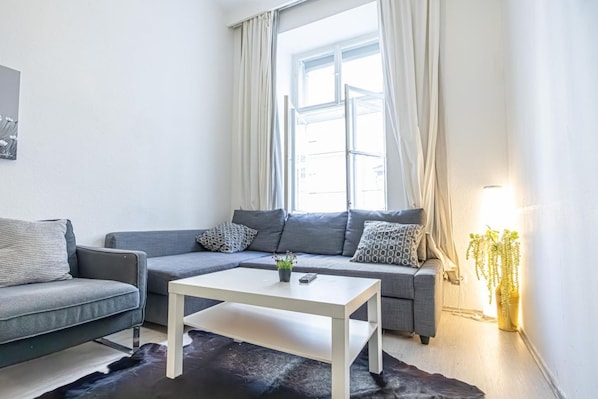 A modern living room with a grey sofa, a white coffee table, and a window with curtains.