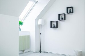 Um quarto com claraboia, luminária de chão e três quadros na parede.
