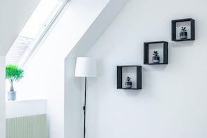 Une pièce dotée d’une lucarne, d’un lampadaire et de trois cadres noirs accrochés au mur.