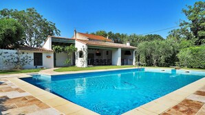 A swimming pool with a tiled deck, a covered patio with outdoor furniture, and a white building with a tiled roof. - Pet friendly home in Moulès (Moulès)
