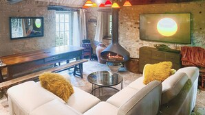 Un salon chaleureux avec un mur en pierre, une cheminée, un ensemble de canapés et un téléviseur à écran plat fixé au mur.