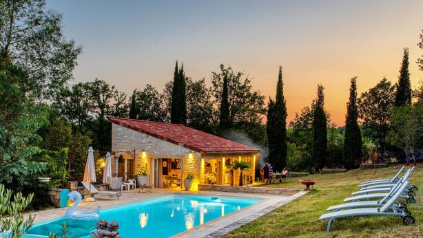 Un bâtiment en pierre avec un toit en tuiles, une piscine et des chaises longues.