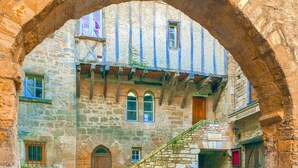 Un bâtiment en pierre avec un étage supérieur à ossature en bois, une porte d’entrée centrale en arc de cercle et un escalier menant à un niveau supérieur.