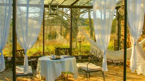 Une véranda avec une table dressée pour deux personnes, entourée de rideaux blancs, et un hamac en arrière-plan.