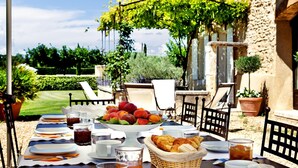 Un espace de restauration en plein air avec une table dressée pour le petit-déjeuner, comprenant des fruits, des viennoiseries et des boissons.