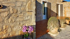 Un edificio de piedra con puerta y ventanas, un pequeño jardín con plantas en macetas y un jarrón de flores.