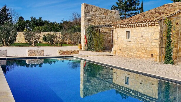 Una piscina con edificios de piedra y árboles al fondo.