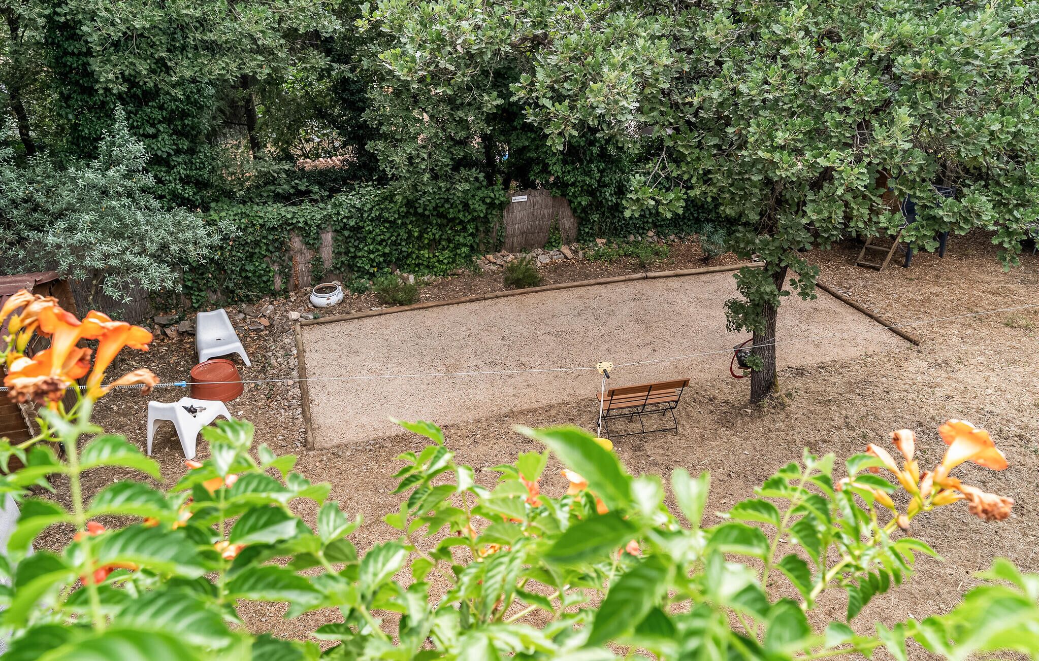 Un jardin clos, aménagé avec un banc, un petit arbre et une chaise en plastique blanche.