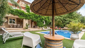 Un pati amb piscina, seients de relaxació blancs, taula de fusta i un parasol de palla.
