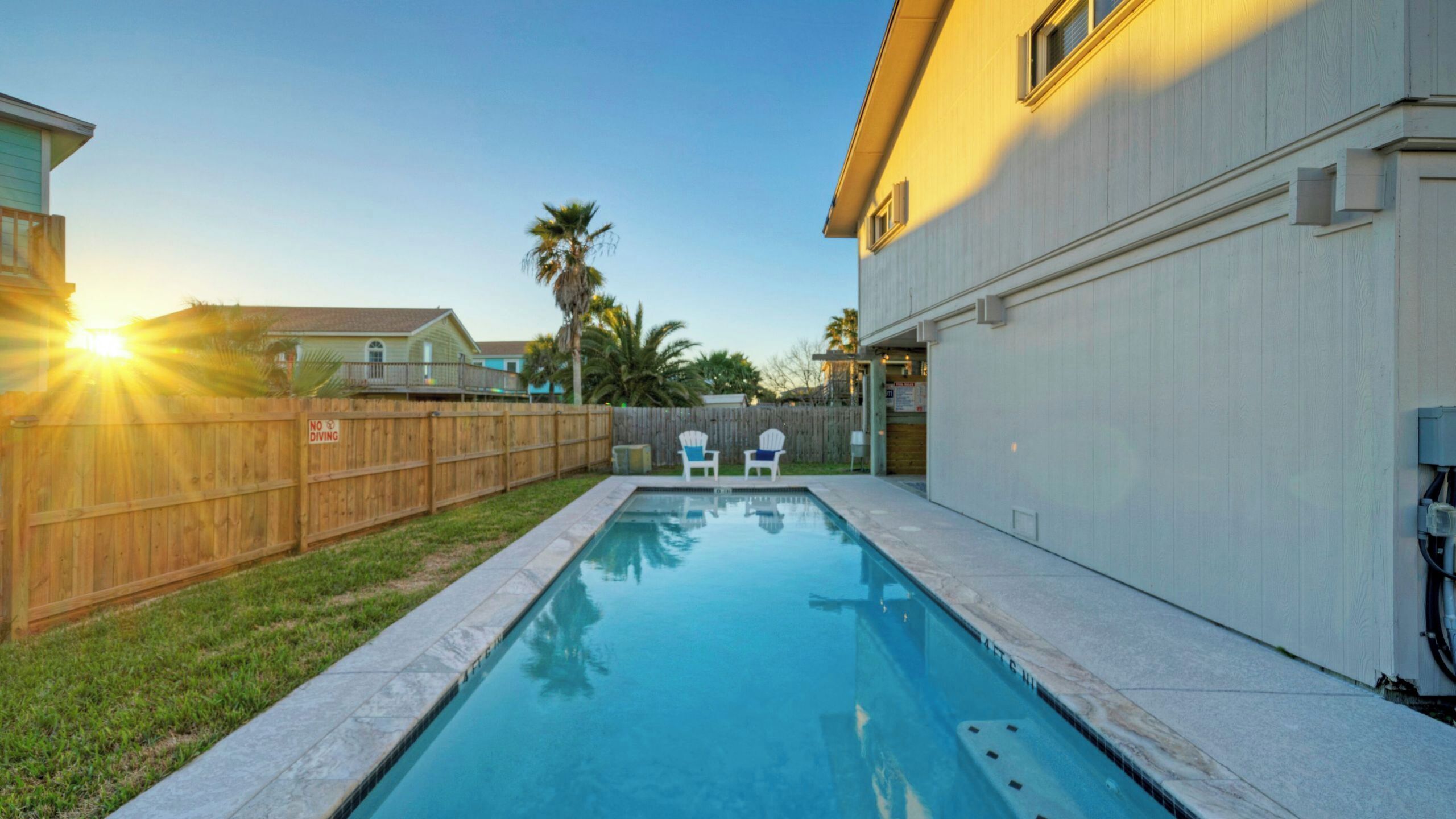 A rectangular swimming pool with a wooden fence and two chairs.