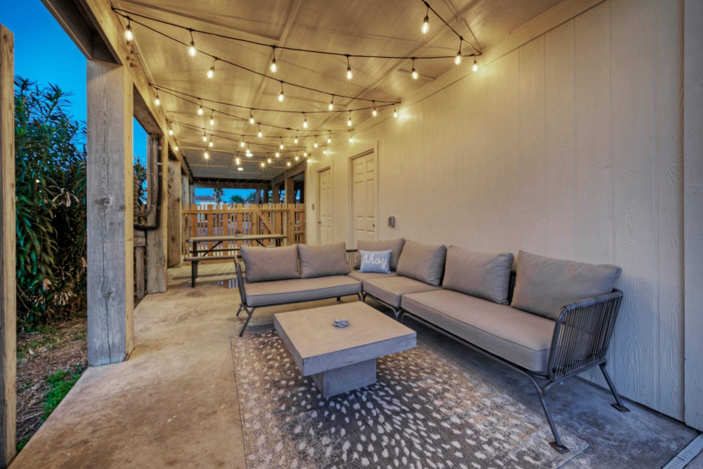 An outdoor living area with a sectional sofa, a coffee table, and string lights.