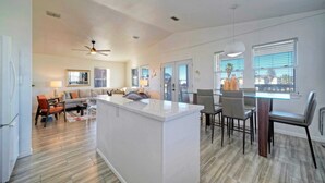 A spacious living area with a central island, a dining area with a glass table, and a kitchen with a white countertop. - Private Pool, in Golf Cart Zone, Golf Cart for Rent Sea Therapy by Avantstay (Port Aransas)