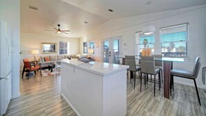 A spacious living area with a central island, a dining area with chairs, and a kitchen with a refrigerator. - Private Pool, in Golf Cart Zone, Golf Cart for Rent Sea Therapy by Avantstay (Port Aransas)