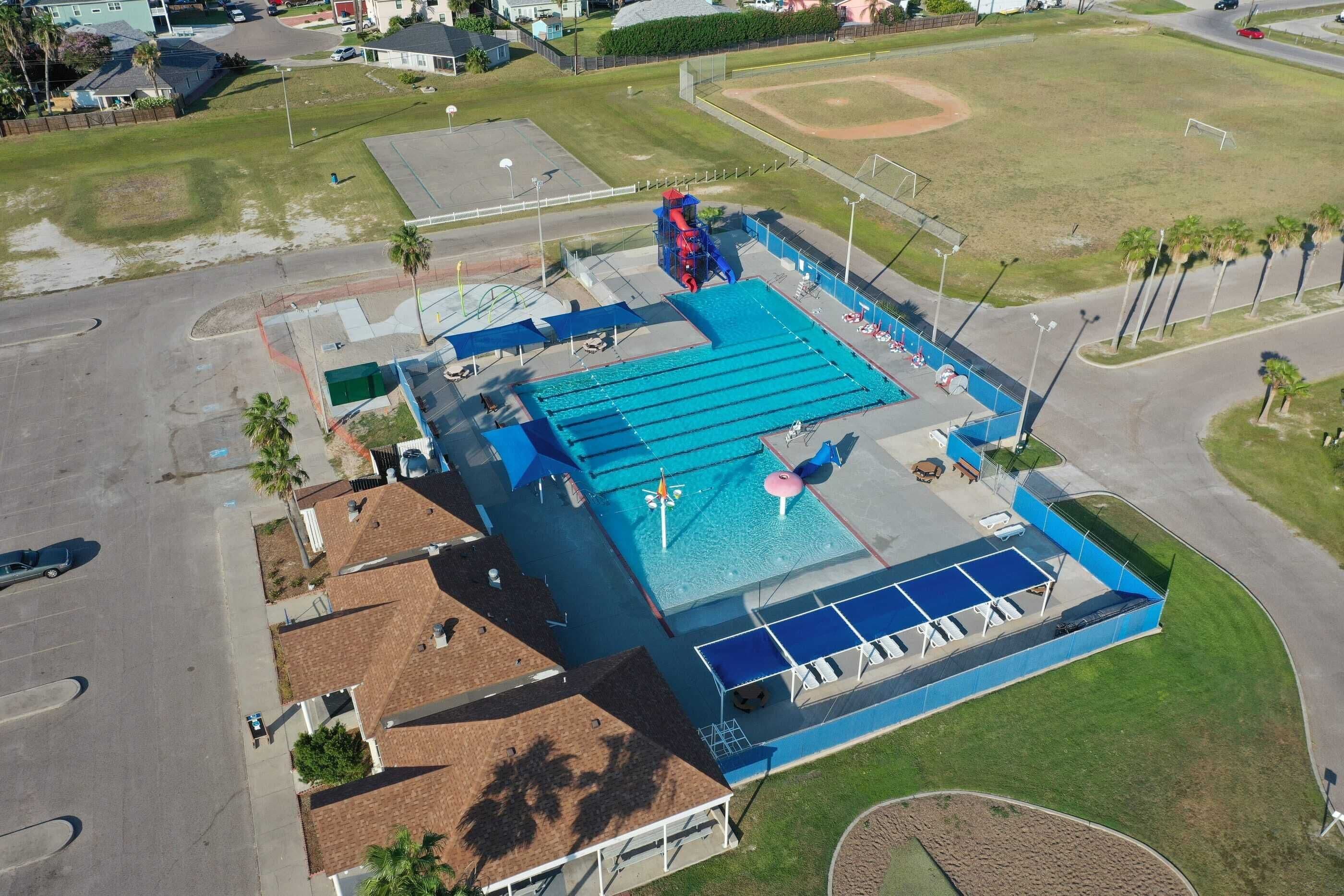 An aerial view of a swimming pool complex with multiple pools, a slide, and a covered area with lounge chairs.