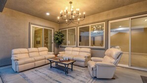 A spacious living room with a chandelier, two sofas, a coffee table, and large windows. - Gated Terra Lago Escape With Private Pool, Hot Tub, Outdoor Kitchen and Lounge (Indio)