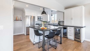 A modern kitchen with a central island, stainless steel appliances, and a large window providing natural light. - Ocean Breeze II by Avantstay Steps to the Beach! (Newport Beach)