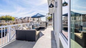 A balcony with wicker furniture, a glass railing, and a view of neighboring buildings. - Ocean Breeze II by Avantstay Steps to the Beach! (Newport Beach)