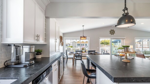 A modern kitchen with a central island, stainless steel appliances, and a large window overlooking a deck. - Ocean Breeze II by Avantstay Steps to the Beach! (Newport Beach)